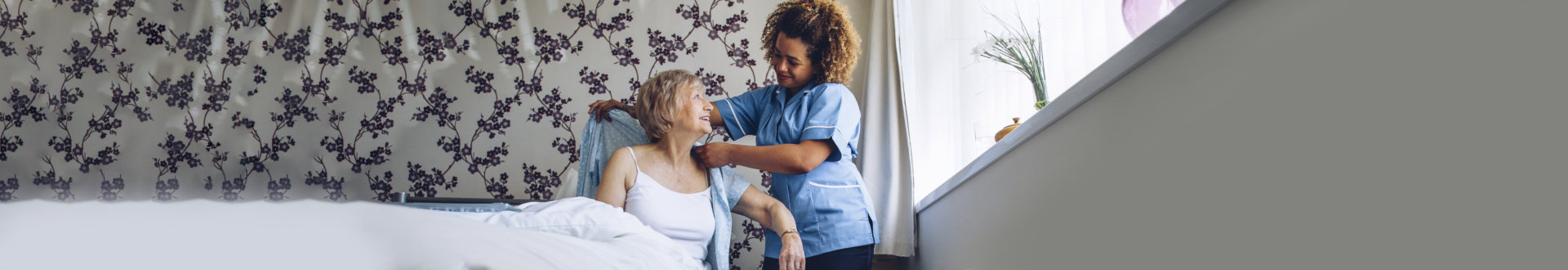 Caregiver helping a senior woman get dressed in her bedroom